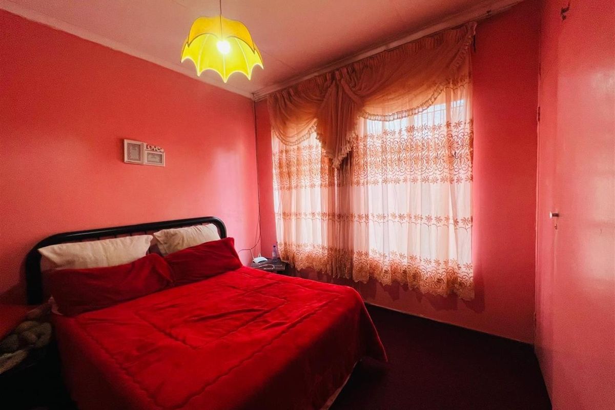 A bedroom featuring pink walls, a window with decorative curtains, and a central pendant light fixture.