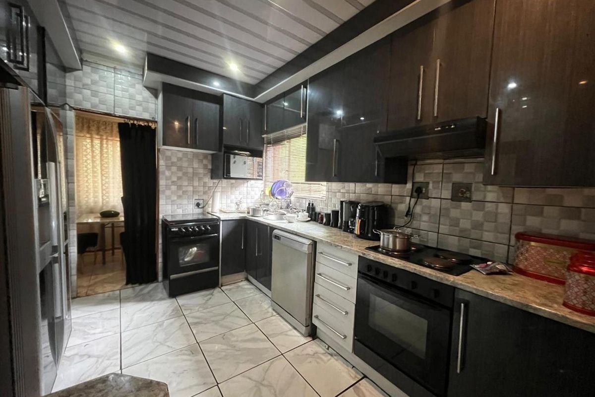 Modern kitchen featuring dark cabinetry, stone-look countertops, built-in oven, hob, and extractor fan with tiled flooring and backsplash.