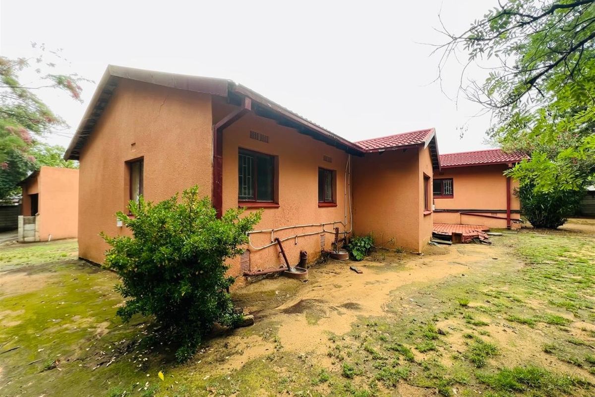 Rear view of the property showing the exterior facade, tiled roof, and surrounding garden area with visible maintenance requirements.
