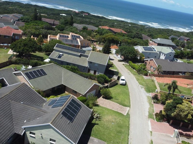 Aerial view of a residential neighborhood featuring homes with solar panel installations, paved roads, and proximity to the coastline.