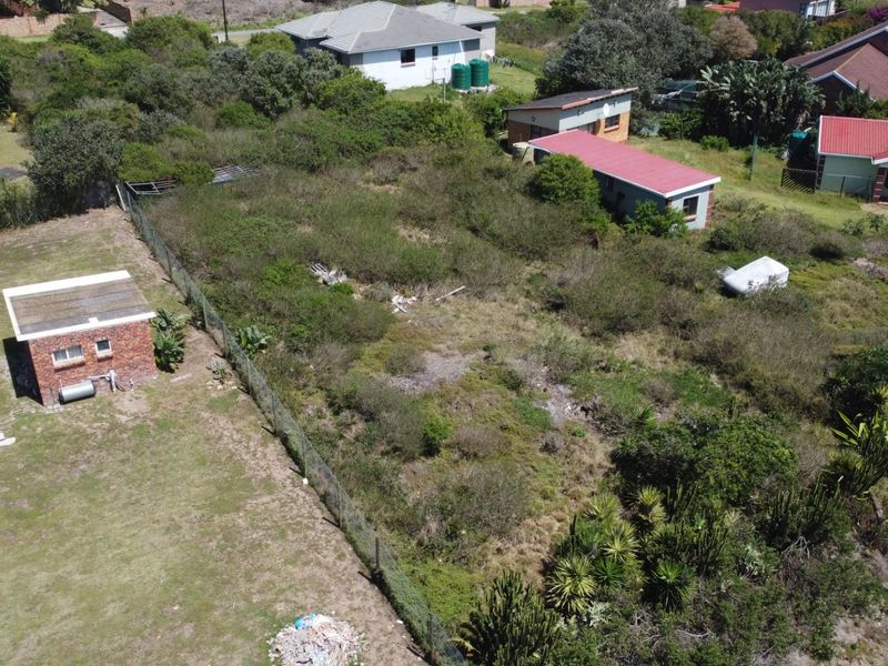 Aerial view of a vacant residential plot featuring established vegetation, a small brick outbuilding, and perimeter fencing in a suburban setting.