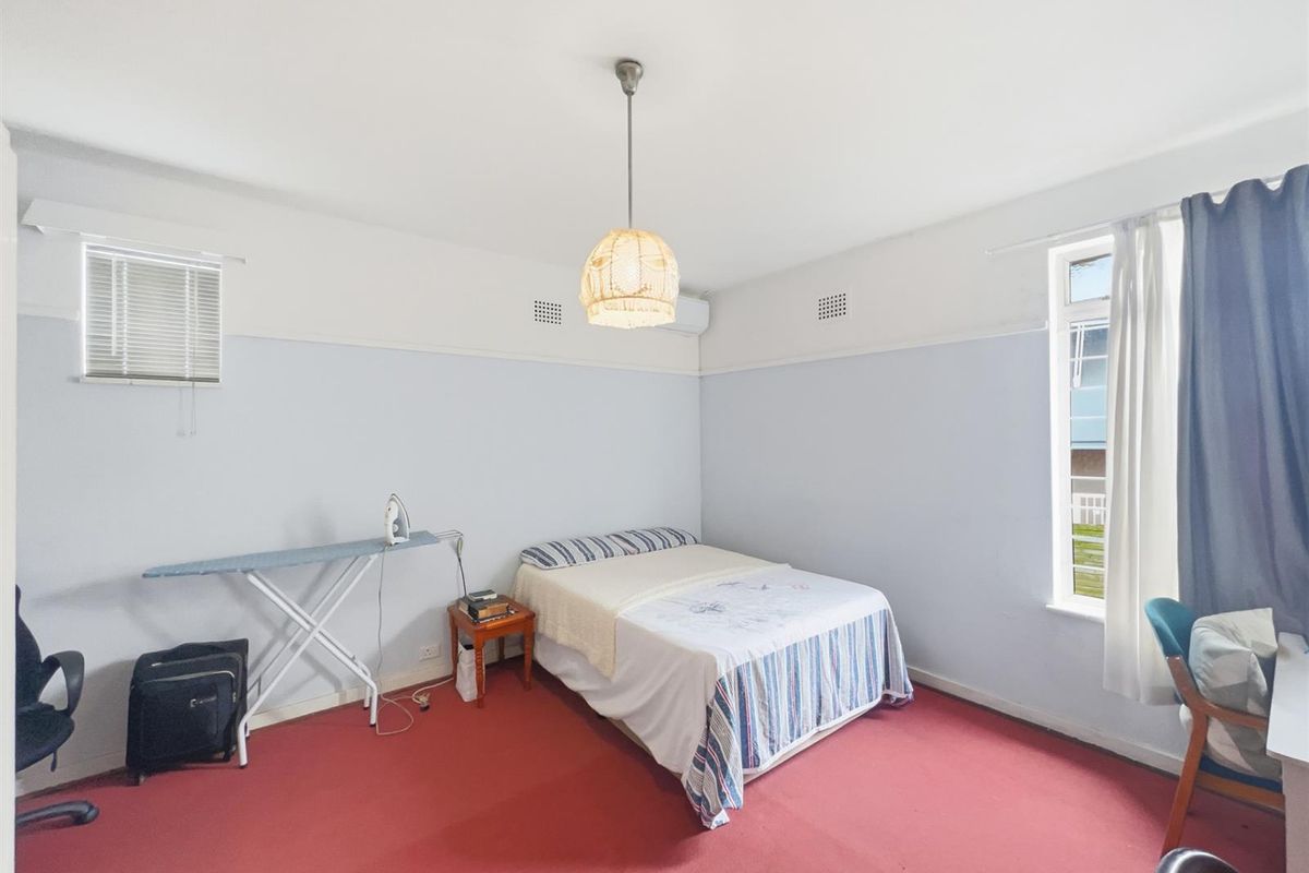 A bedroom featuring red carpeting, a wall-mounted air conditioning unit, and natural light from the window.