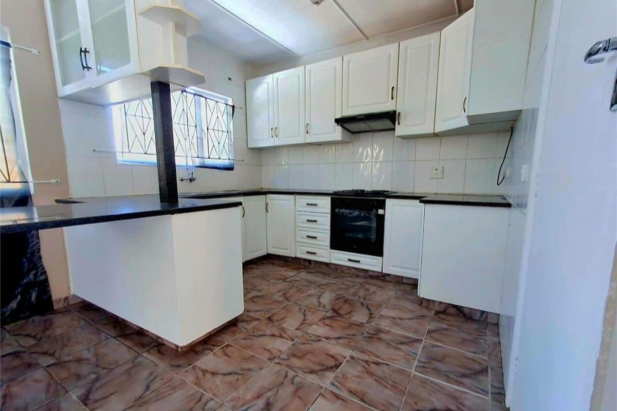 A functional kitchen featuring white built-in cabinetry, dark granite countertops, a built-in oven, hob, and extractor fan with tiled flooring throughout.