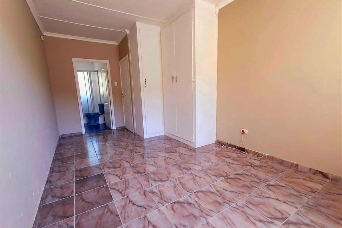 An empty bedroom featuring tiled flooring, built-in cupboards, and direct access to an adjacent bathroom.