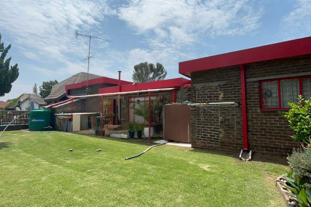 Rear view of the property featuring a brick facade, red metal roof trim, and a spacious lawn area with a water tank.
