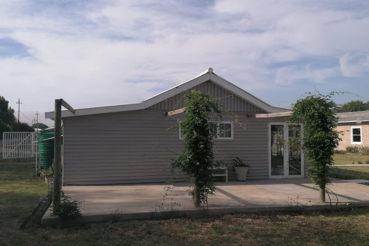 Rear view of the property featuring a concrete patio area, timber pergola structure, and glass sliding doors leading into the building.