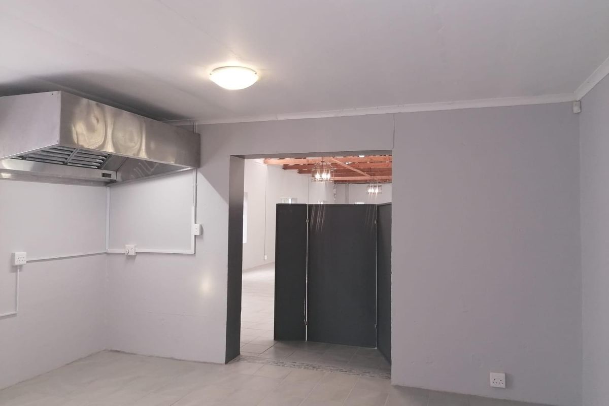 Commercial kitchen area featuring a stainless steel extractor hood, tiled flooring, and a partitioned doorway leading to an open-plan space.