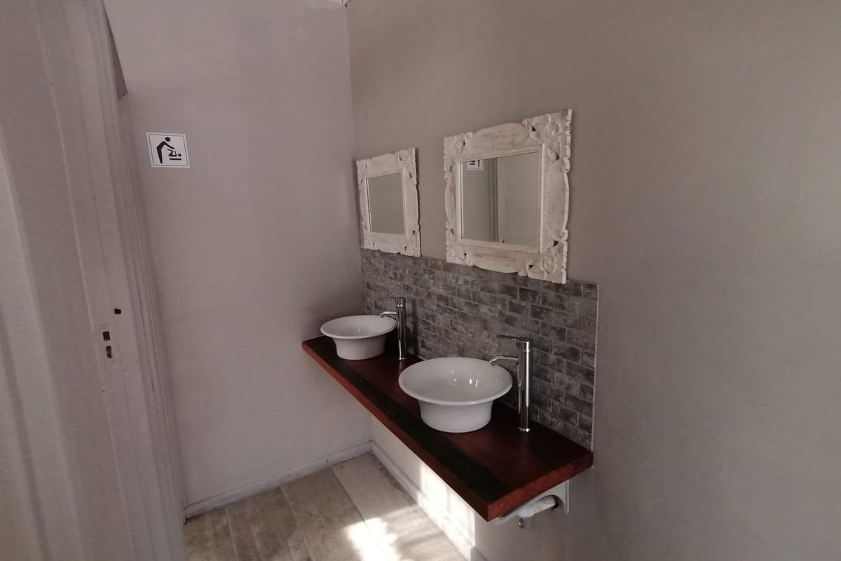 A functional bathroom vanity area featuring dual vessel sinks mounted on a wooden countertop with a tiled backsplash and wall-mounted mirrors.