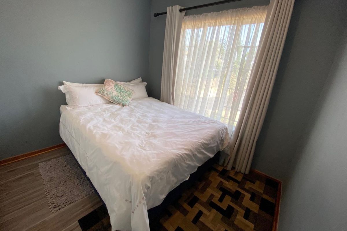 A bedroom featuring blue-toned walls, a large window with curtain rod, and mixed flooring finishes.
