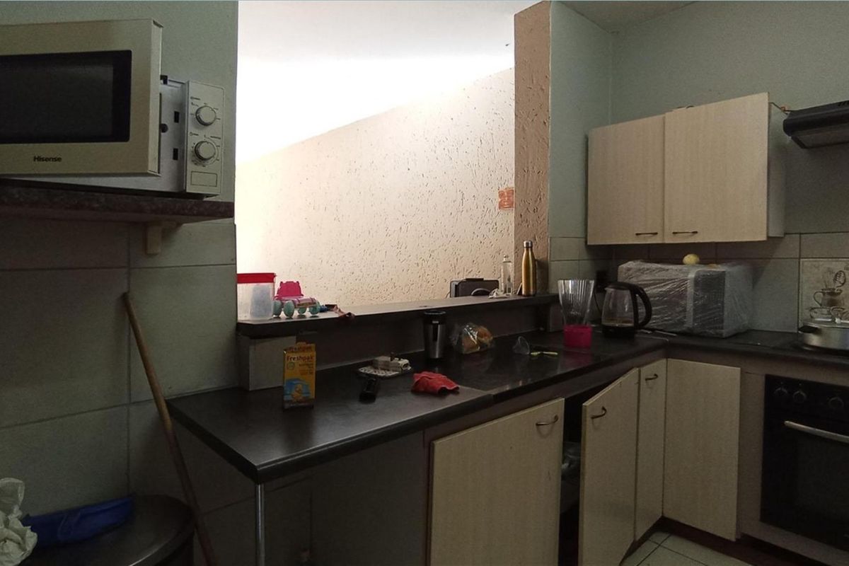 Functional kitchen featuring dark laminate countertops, light-toned cabinetry, built-in oven, extractor fan, and a breakfast bar opening to the adjacent living area.