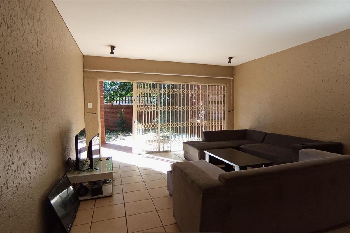 A living room featuring tiled flooring and a sliding door with security gate leading to an outdoor area.