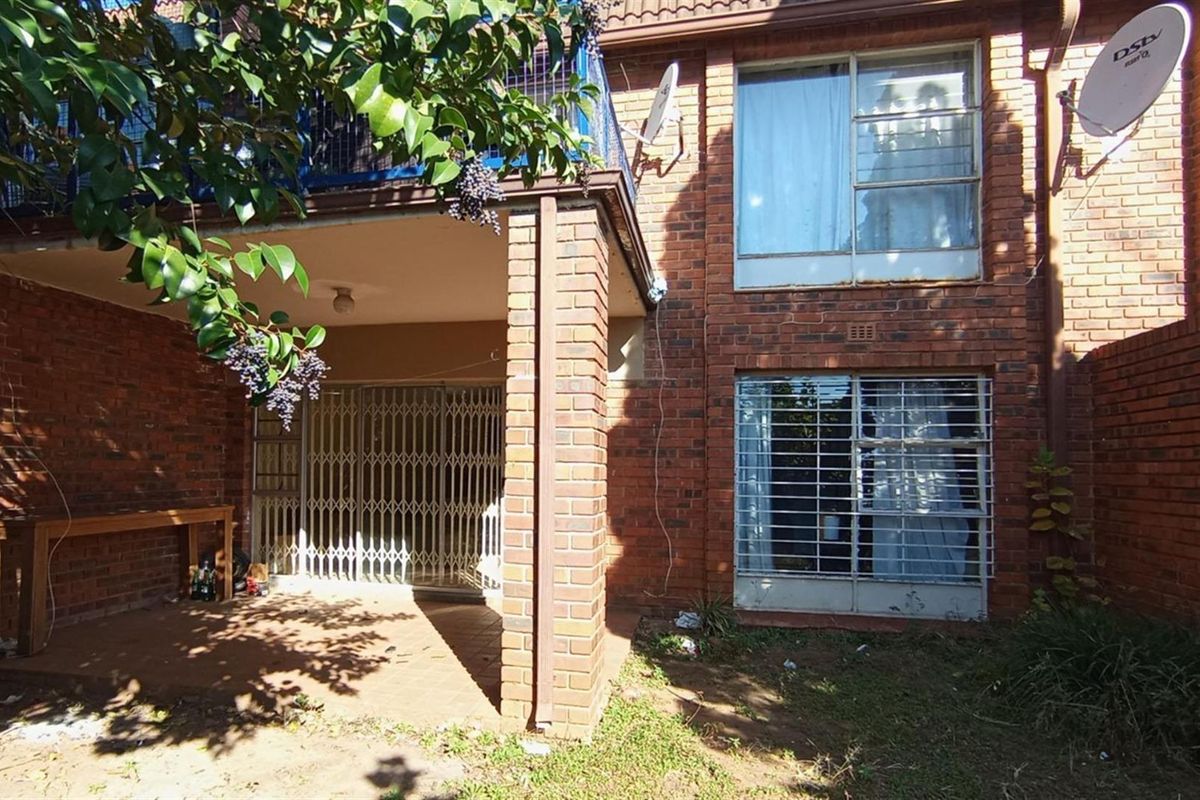 Rear view of the apartment featuring a covered patio area, brick facade, and security gates on windows and doors.