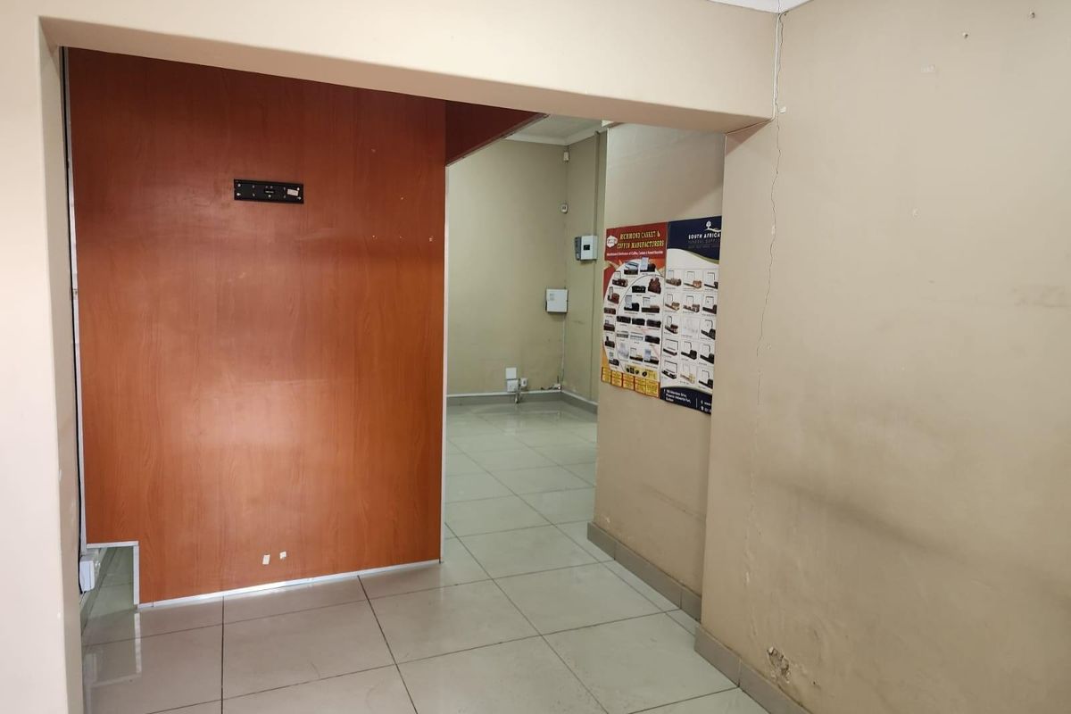 An empty commercial interior space featuring tiled flooring, a wood-panelled partition wall, and visible electrical points.