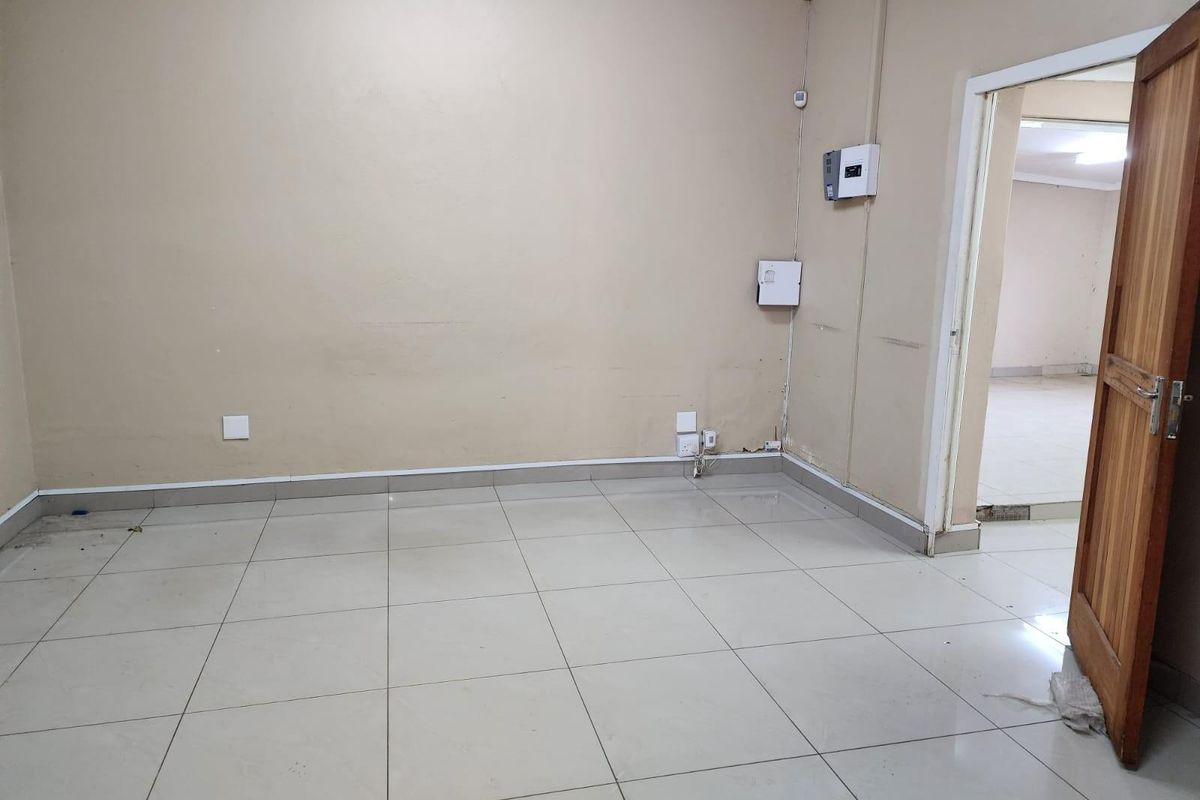 An empty office space featuring neutral wall tones, tiled flooring, and visible electrical distribution boards, providing a functional blank canvas for business operations.