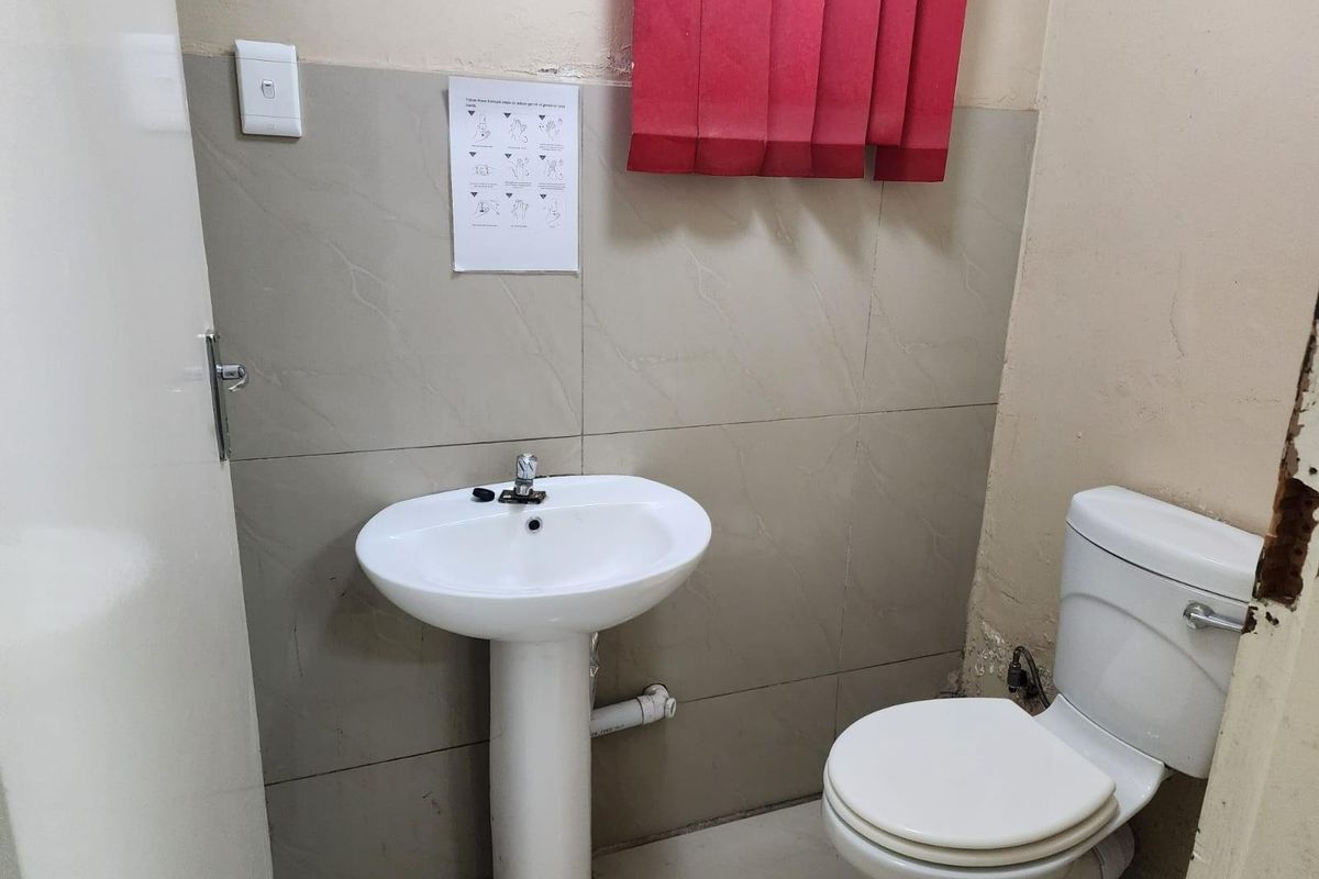 A compact bathroom featuring a pedestal basin and a standard toilet with tiled splashback walls.