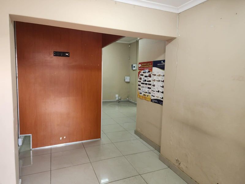 An empty commercial interior space featuring tiled flooring, a wood-panelled partition wall, and visible electrical points.