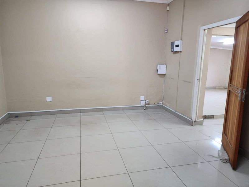 An empty office space featuring neutral wall tones, tiled flooring, and visible electrical distribution boards, providing a functional blank canvas for business operations.