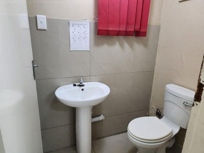 A compact bathroom featuring a pedestal basin and a standard toilet with tiled splashback walls.