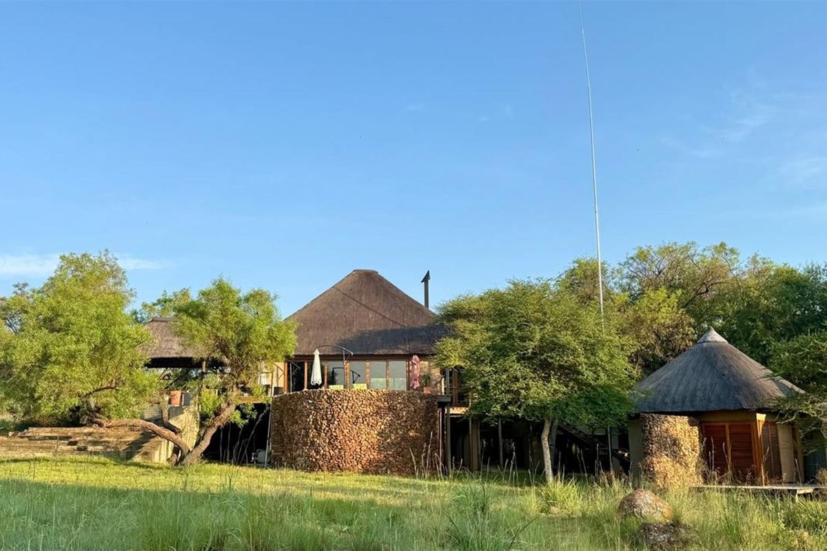 Rear view of a bushveld-style property featuring traditional thatched roofing, natural stone cladding, and an elevated wooden deck set within a natural landscape.