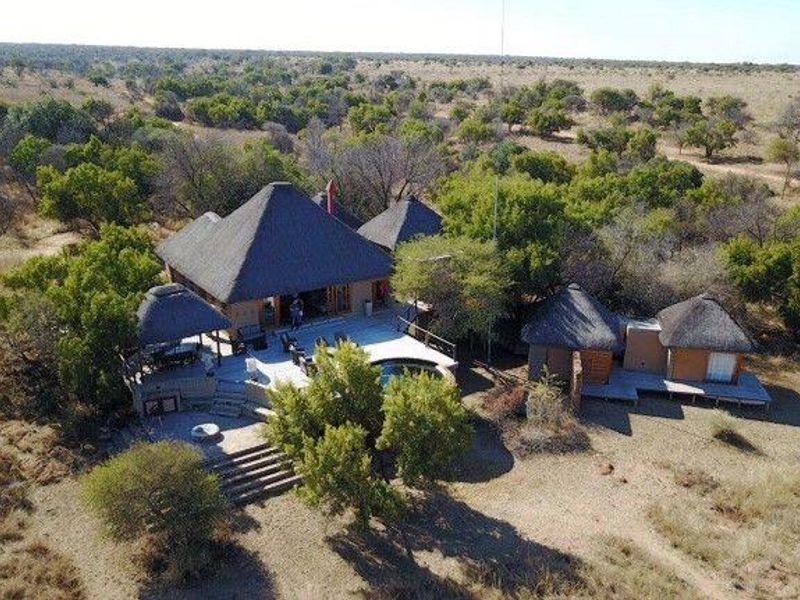 Aerial view of a bushveld lodge featuring multiple thatched-roof structures, a central swimming pool, and extensive timber decking set within a natural landscape.
