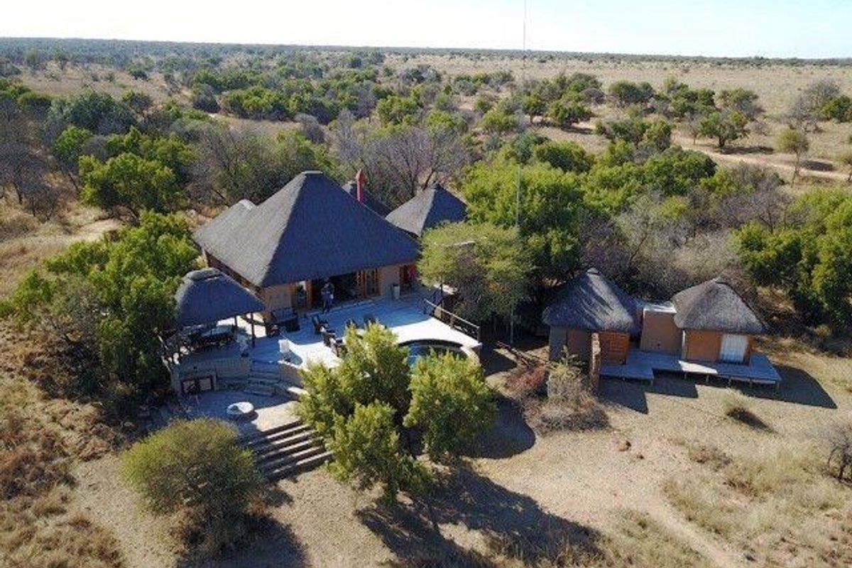 Aerial view of a bushveld lodge featuring multiple thatched-roof structures, a central swimming pool, and extensive timber decking set within a natural landscape.