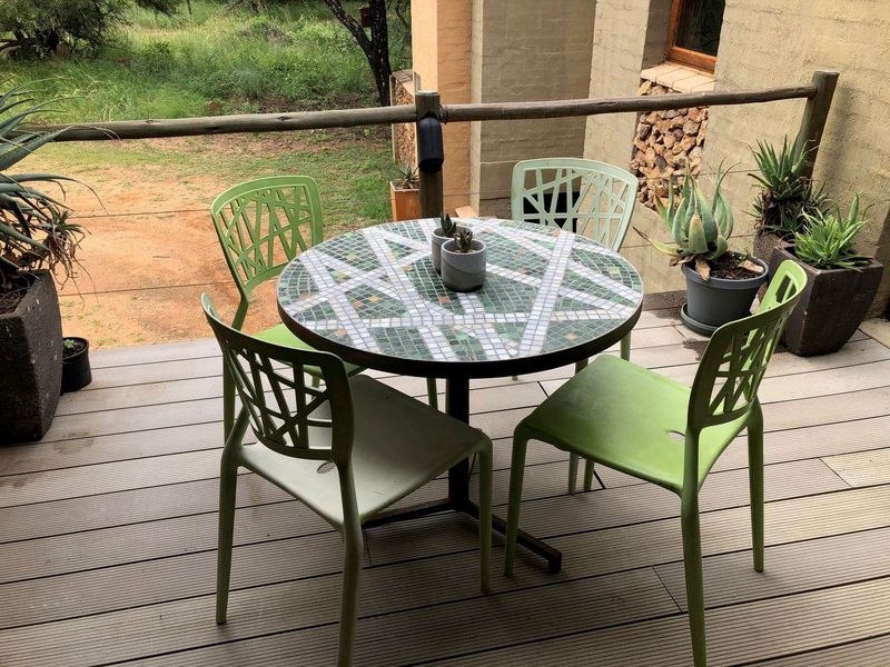 A covered outdoor patio area featuring timber decking and a rustic timber railing, overlooking a natural garden setting.