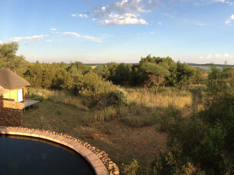 Outdoor pool area featuring a circular swimming pool with stone coping, adjacent timber decking, and views of surrounding thatched structures and natural landscape.