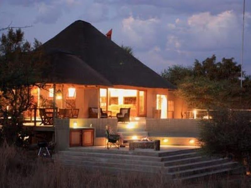 A charming lodge-style property featuring a thatched roof, expansive concrete patio, and a built-in fire pit, perfect for evening outdoor relaxation.