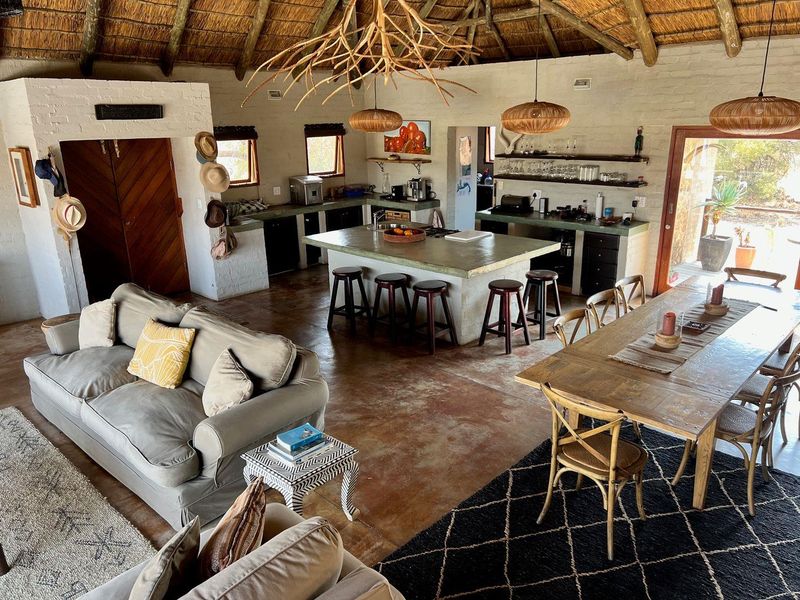 Spacious open-plan living area featuring a rustic thatched roof, exposed brick walls, concrete flooring, and a central kitchen island with integrated cabinetry.