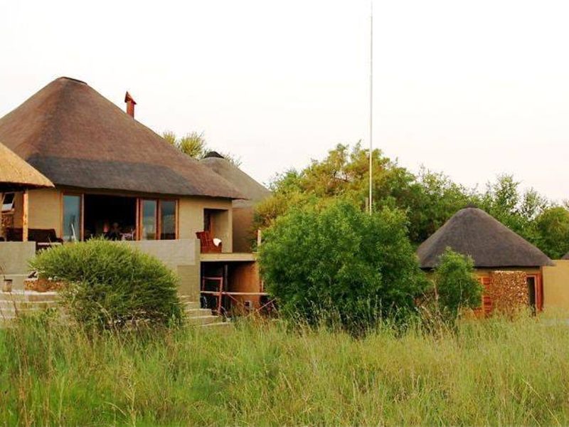 A rear view of a commercial property featuring multiple structures with traditional thatch roofs, concrete patios, and natural stone accents set in a landscape.