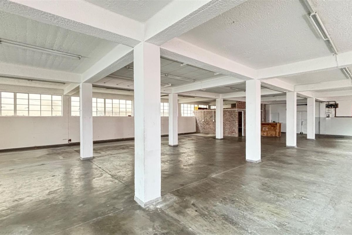 Expansive open-plan commercial space featuring industrial concrete flooring, exposed structural columns, and large windows providing ample natural light.