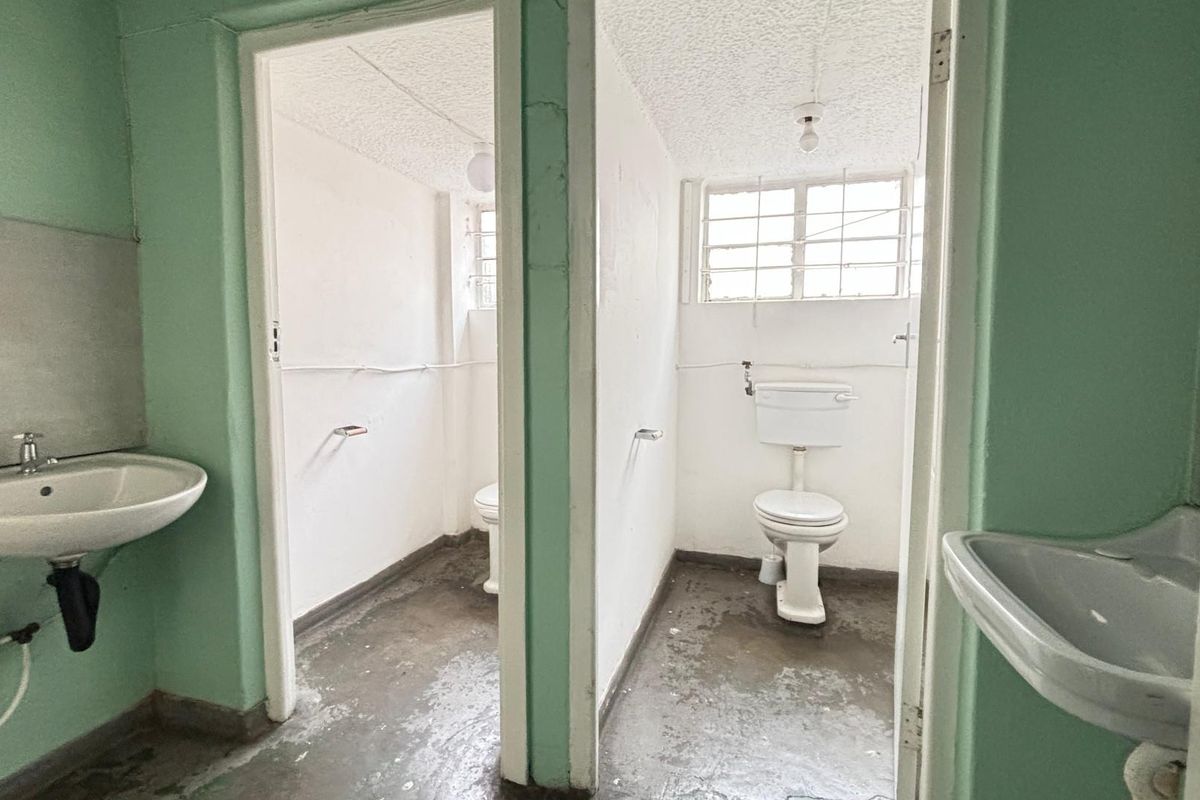 A commercial restroom facility featuring two separate toilet cubicles and two wall-mounted washbasins with basic finishes.