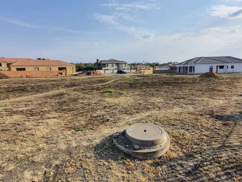 A vacant residential plot featuring a level surface, a visible manhole cover, and surrounding boundary walls in an established residential estate.