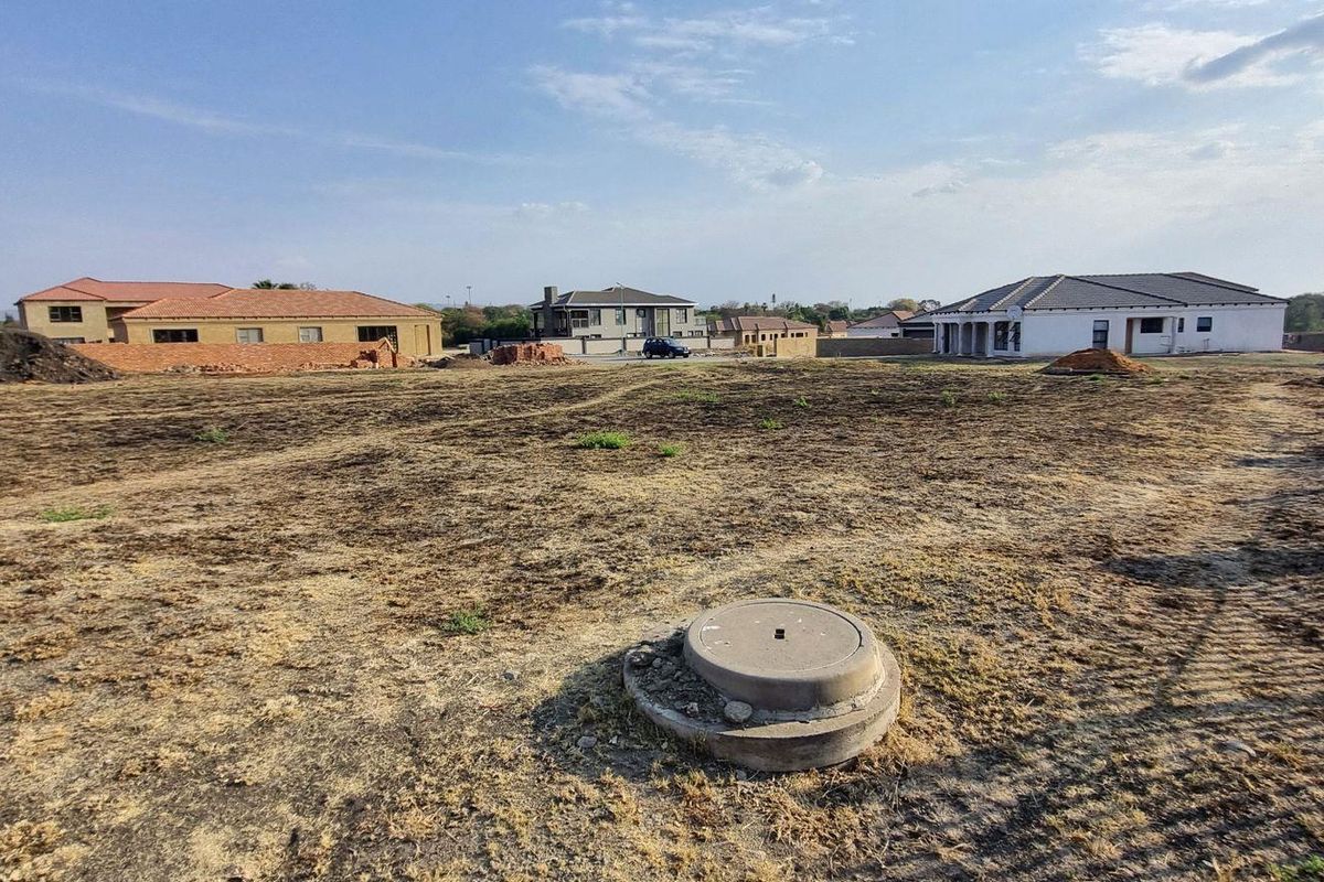 A vacant residential plot featuring a level surface, a visible manhole cover, and surrounding boundary walls in an established residential estate.