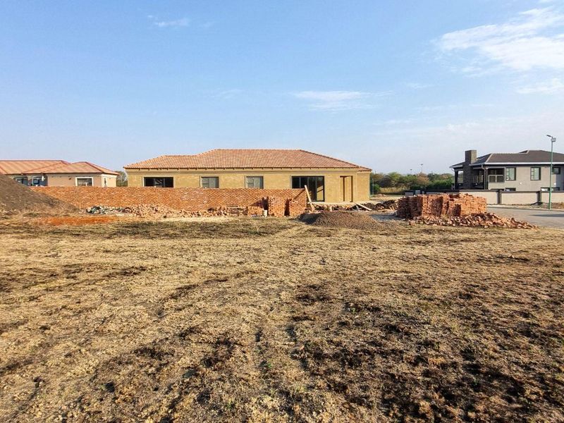 A view of a vacant residential plot featuring uneven ground, construction materials, and a partial brick boundary wall in a developing neighborhood.