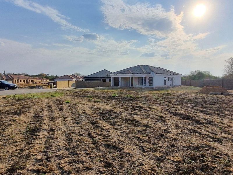 A view of a vacant residential plot in a developing estate, featuring surrounding boundary walls and nearby residential housing.