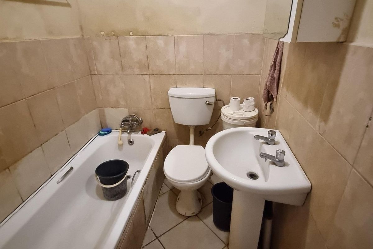 A compact bathroom featuring a standard bathtub, pedestal basin, and toilet, requiring cosmetic updates and refurbishment to improve its overall condition.