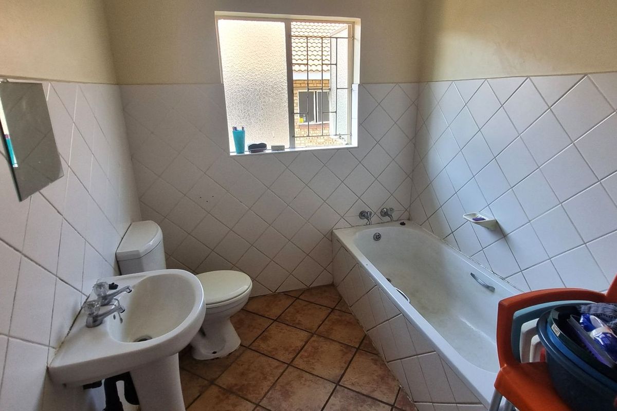 A functional bathroom featuring a pedestal basin, toilet, and bathtub with diamond-patterned wall tiling and tiled flooring.