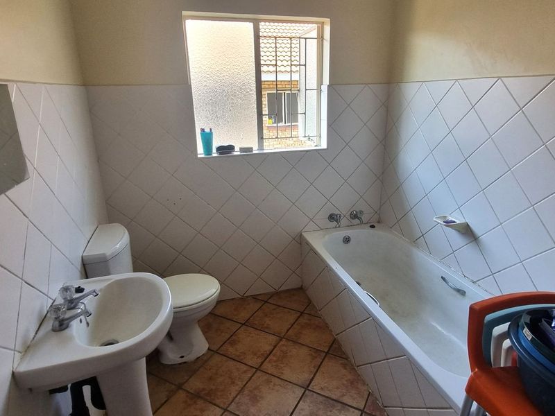 A functional bathroom featuring a pedestal basin, toilet, and bathtub with diamond-patterned wall tiling and tiled flooring.