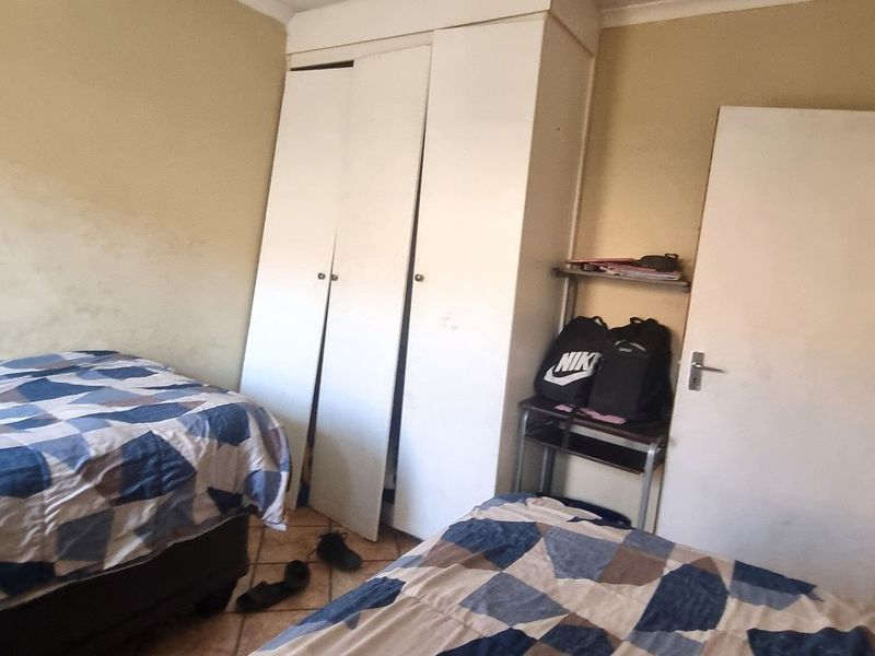 A bedroom featuring tiled flooring and a built-in wardrobe. The room requires cosmetic updates to the wall finishes to improve its overall condition.