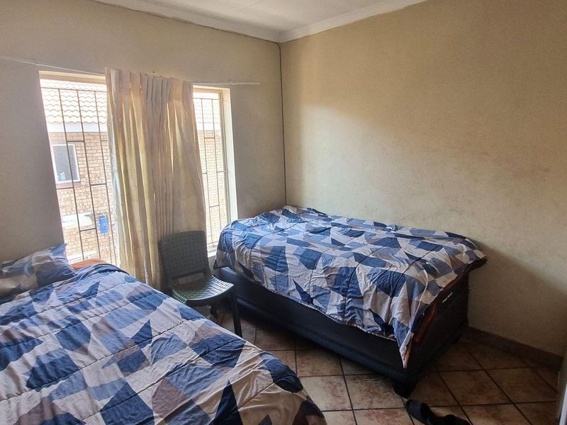 A bedroom featuring tiled flooring, security bars on the window, and a built-in cupboard, requiring cosmetic updates to the wall finishes.