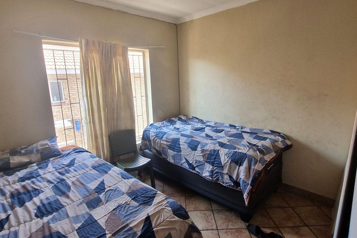 A bedroom featuring tiled flooring, security bars on the window, and a built-in cupboard, requiring cosmetic updates to the wall finishes.