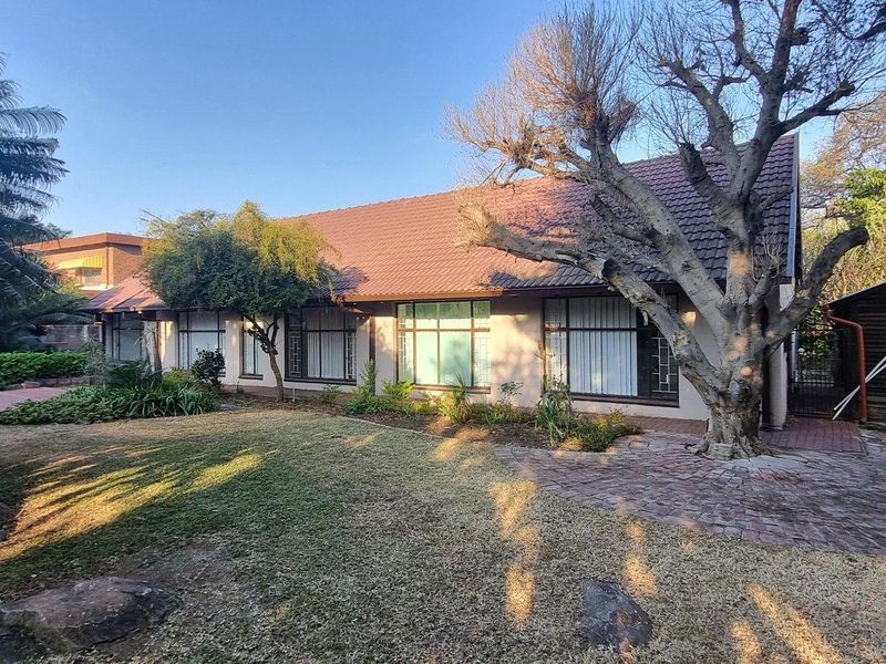 Rear view of the property featuring a tiled roof, paved patio area, and a detached wooden storage shed set within a landscaped garden.