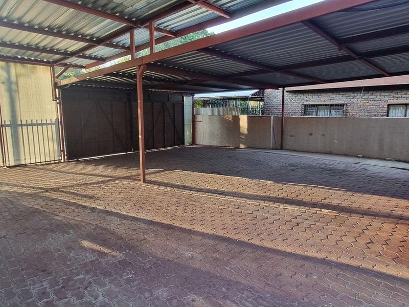 A spacious covered carport or garage area featuring a durable corrugated metal roof, steel support structure, and paved flooring.