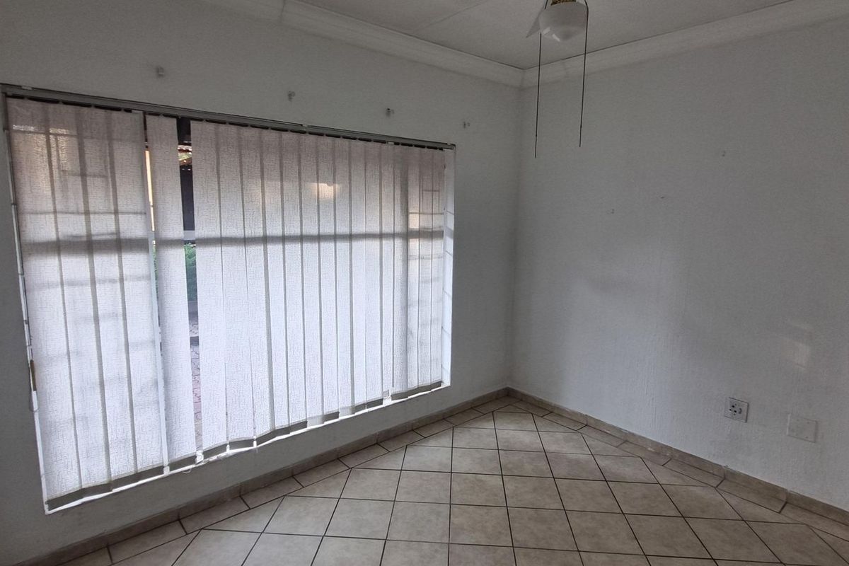 An empty bedroom featuring tiled flooring, vertical blinds, and a ceiling light fixture, ready for a fresh coat of paint and new interior design.