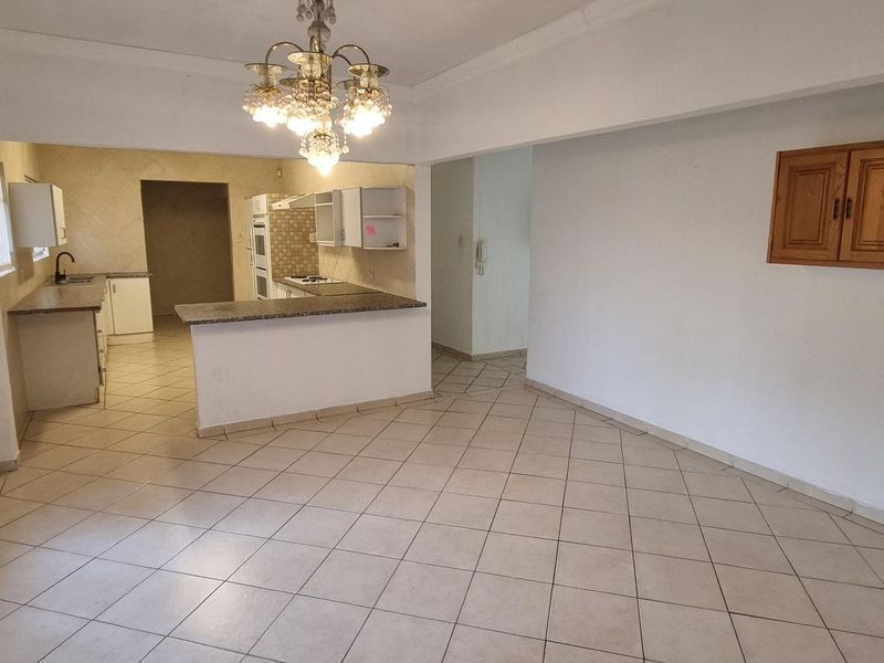 An open-plan living and kitchen area featuring tiled flooring, a breakfast bar, and built-in kitchen cabinetry.
