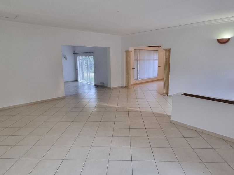 A spacious, empty living area featuring neutral ceramic floor tiles, decorative columns, and access to an adjoining room through a sliding glass door.