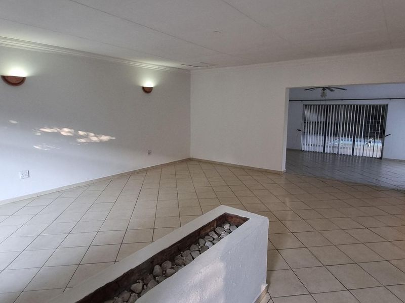 A spacious, empty living area featuring tiled floors, wall-mounted lighting, and a decorative column, leading into an adjacent room with sliding glass doors.