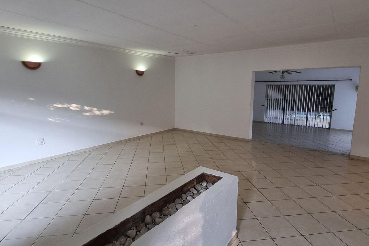 A spacious, empty living area featuring tiled floors, wall-mounted lighting, and a decorative column, leading into an adjacent room with sliding glass doors.