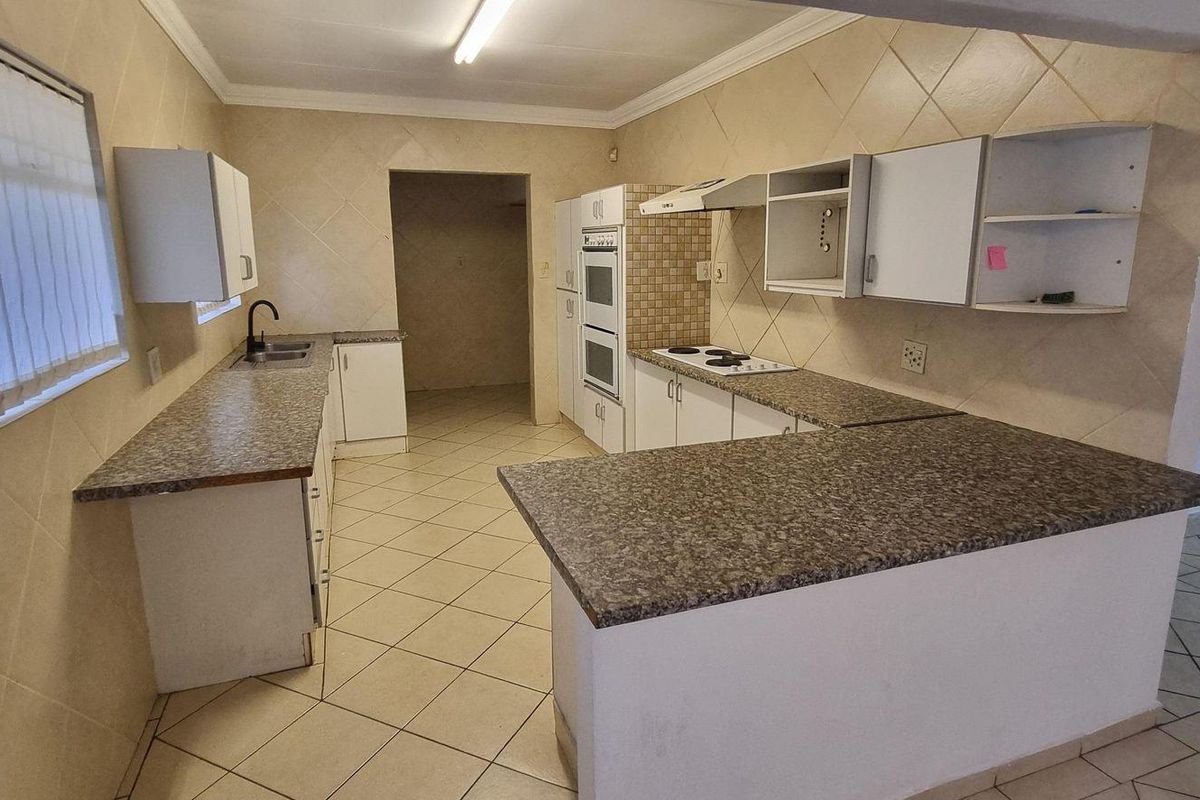A functional kitchen featuring granite countertops, built-in eye-level oven, hob, extractor fan, and tiled finishes throughout, offering a practical layout for culinary activities.